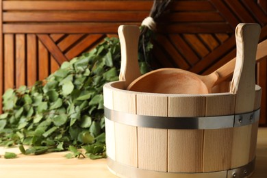 Photo of Sauna equipment. Bucket, ladle and birch whisk on wooden surface, closeup