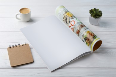 Open magazine with blank page, coffee, plant and notebook on white wooden table. Mockup for design