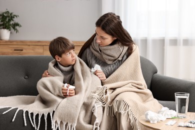 Cold symptom. Woman with her son suffering from fever on sofa at home