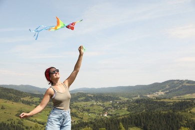 Photo of Smiling woman flying kite in mountains under blue sky. Space for text