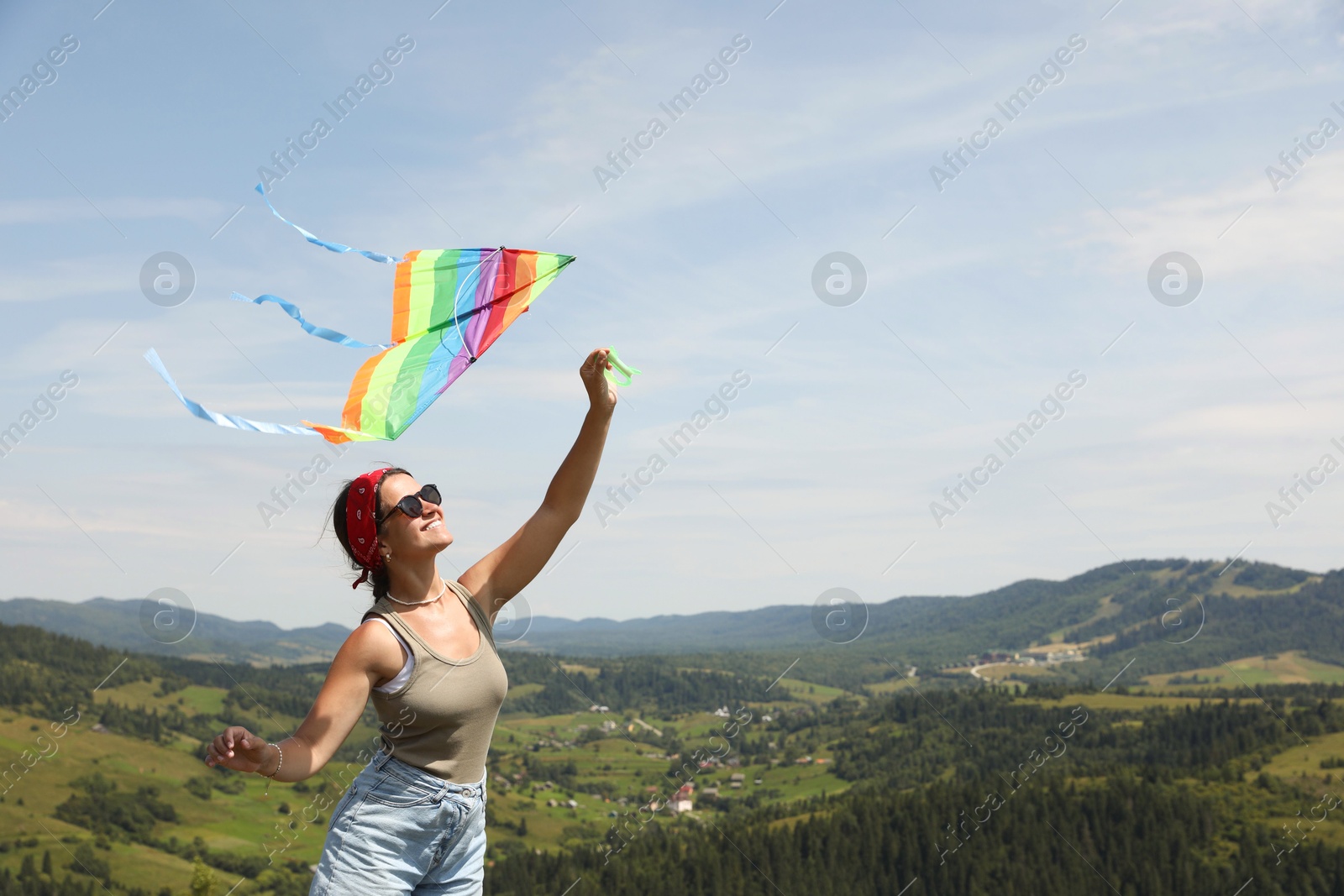 Photo of Smiling woman flying kite in mountains under blue sky. Space for text