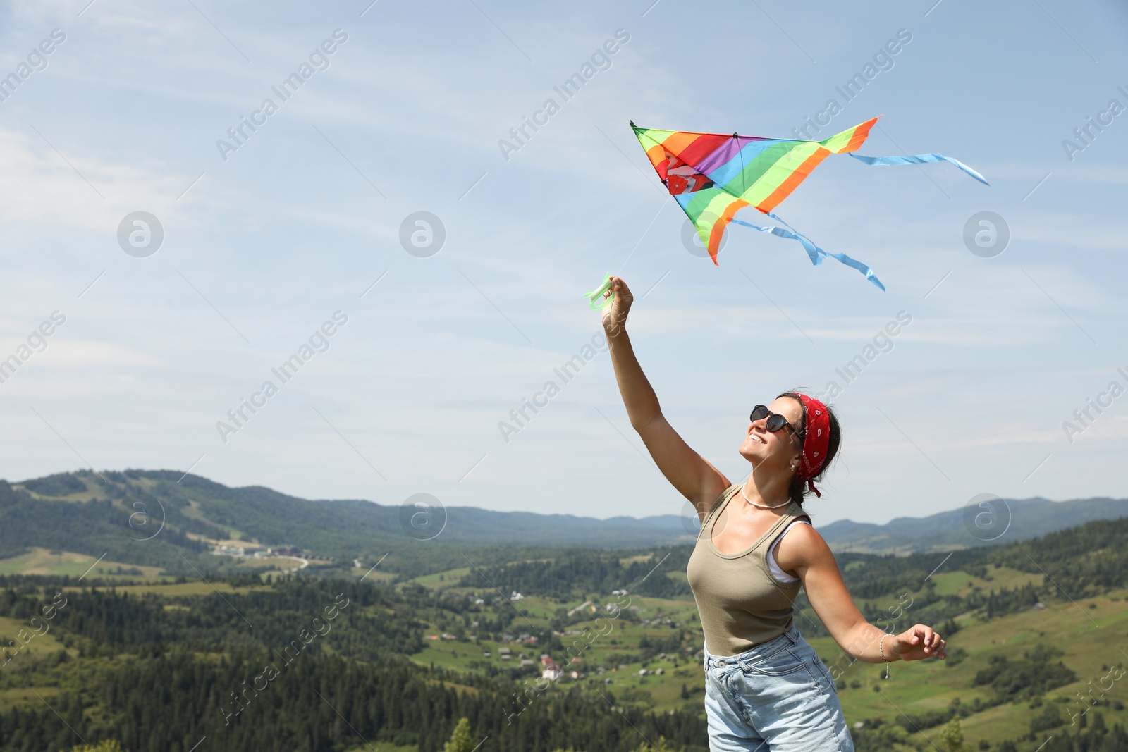 Photo of Smiling woman flying kite in mountains under blue sky. Space for text