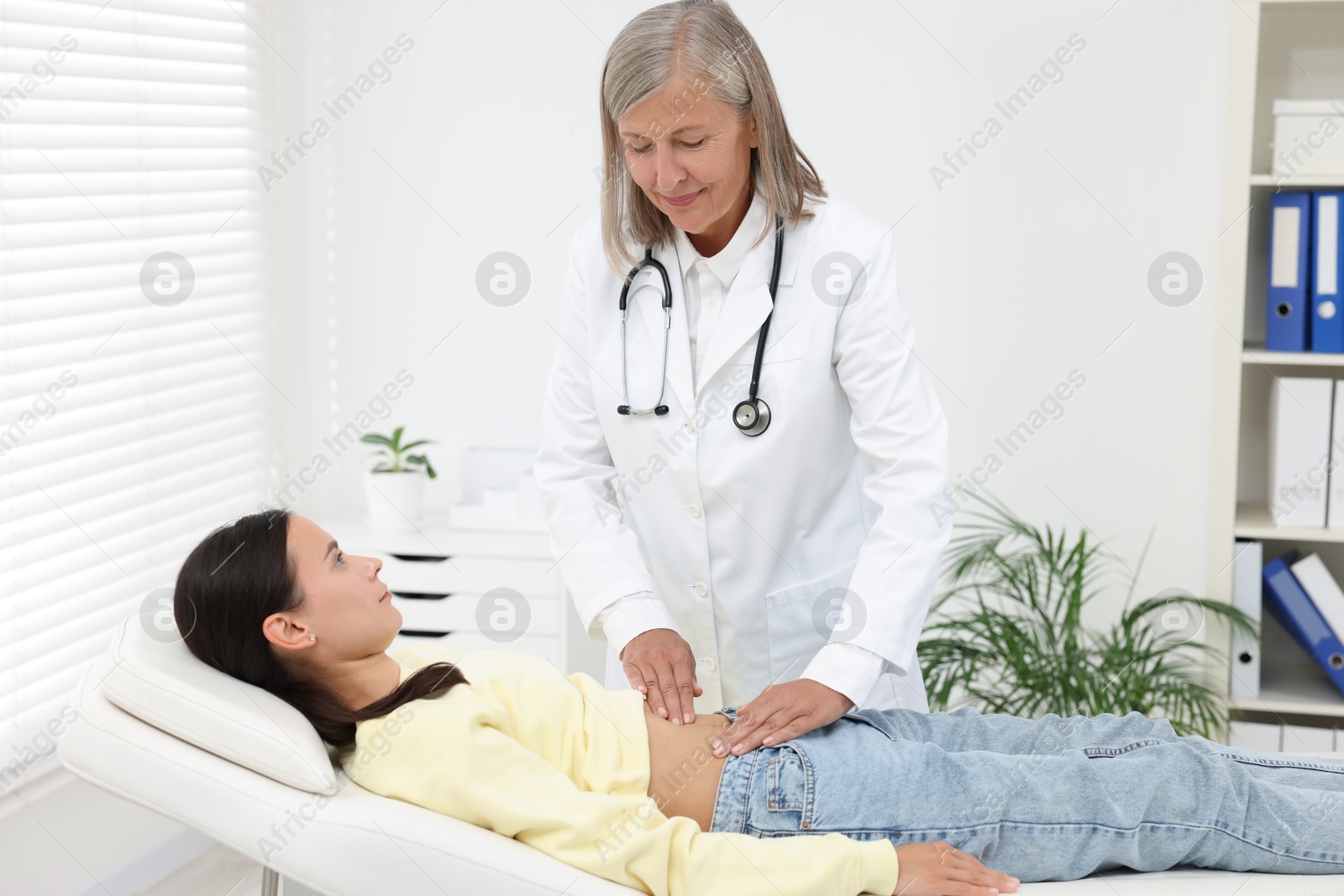 Photo of Doctor examining woman with stomach pain on couch in clinic