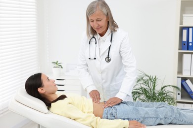 Photo of Doctor examining woman with stomach pain on couch in clinic