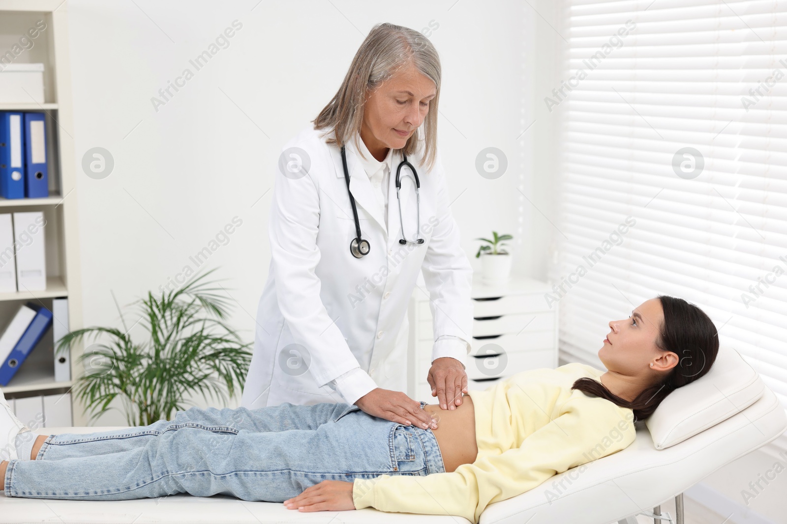 Photo of Doctor examining woman with stomach pain on couch in clinic