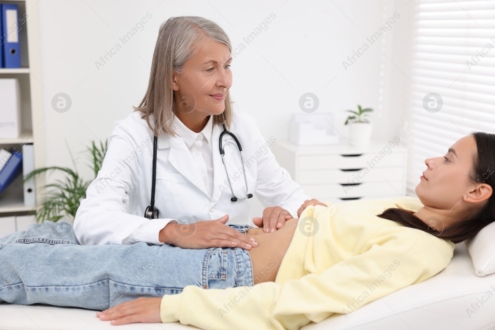 Photo of Doctor examining woman with stomach pain on couch in clinic