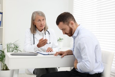 Photo of Doctor consulting patient with stomach pain at table in clinic