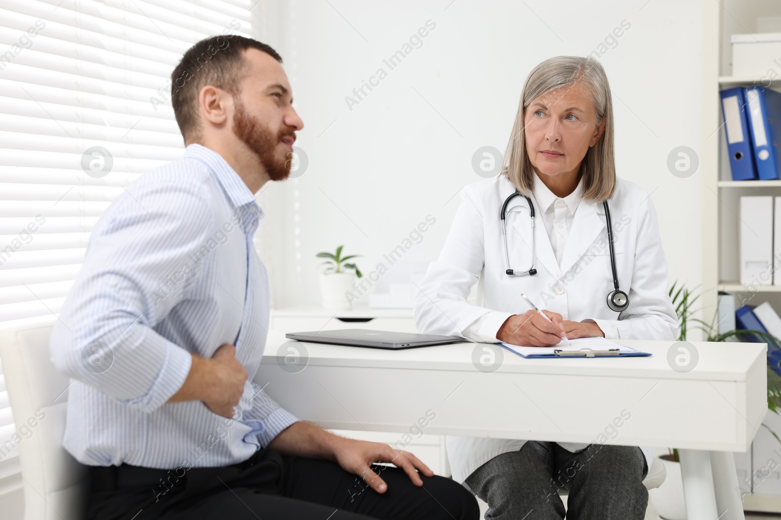 Photo of Doctor consulting patient with stomach pain at table in clinic