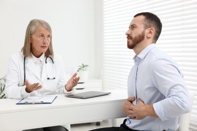 Photo of Doctor consulting patient with stomach pain at table in clinic