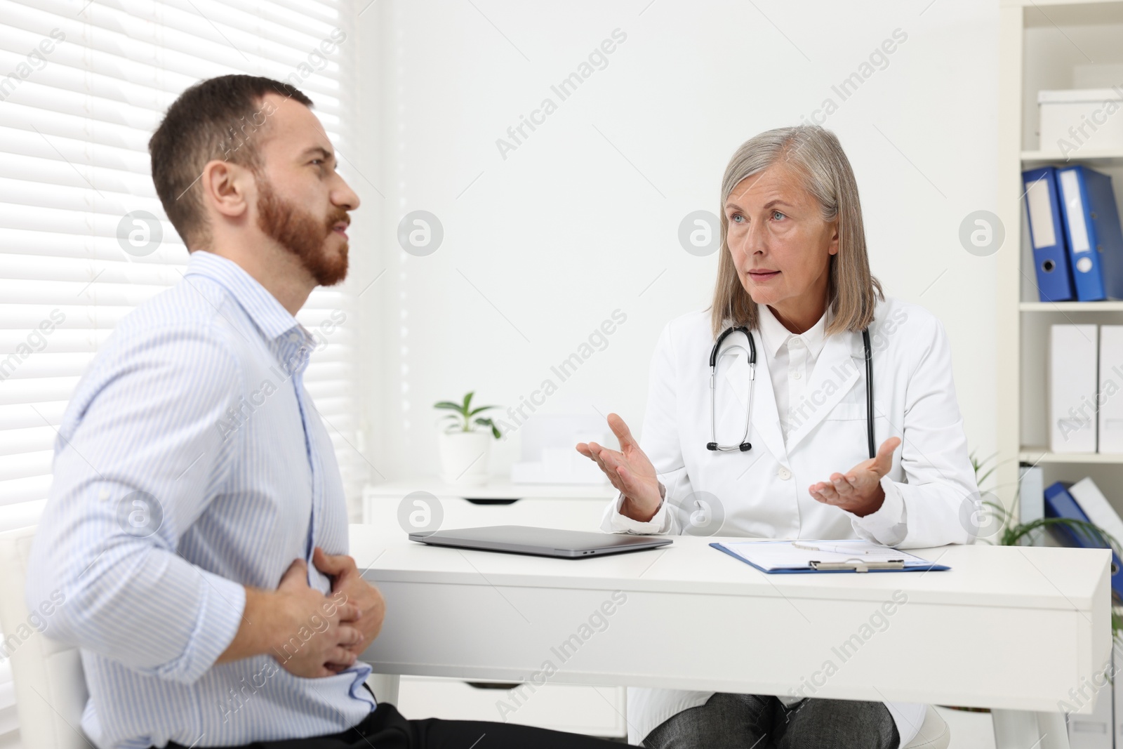 Photo of Doctor consulting patient with stomach pain at table in clinic