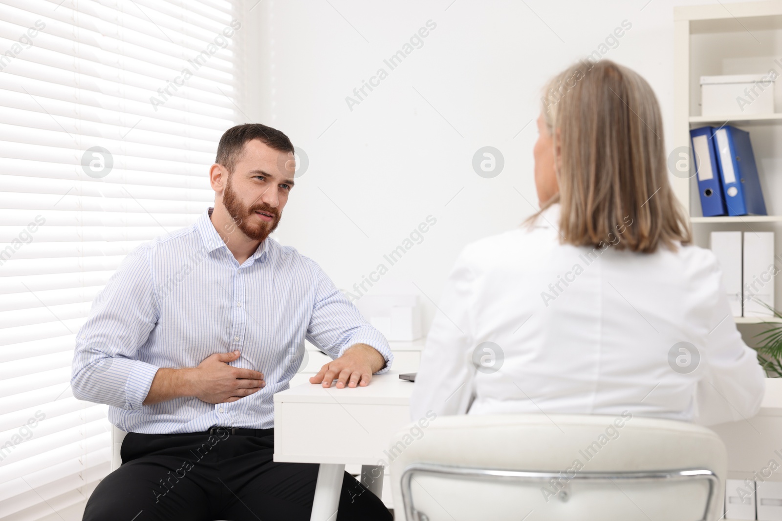 Photo of Doctor consulting patient with stomach pain at table in clinic, back view