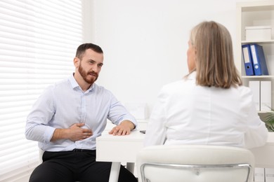 Photo of Doctor consulting patient with stomach pain at table in clinic, back view