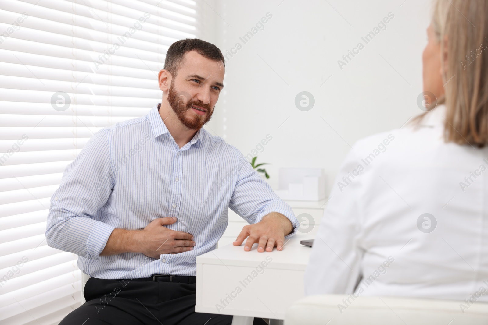 Photo of Doctor consulting patient with stomach pain at table in clinic, back view