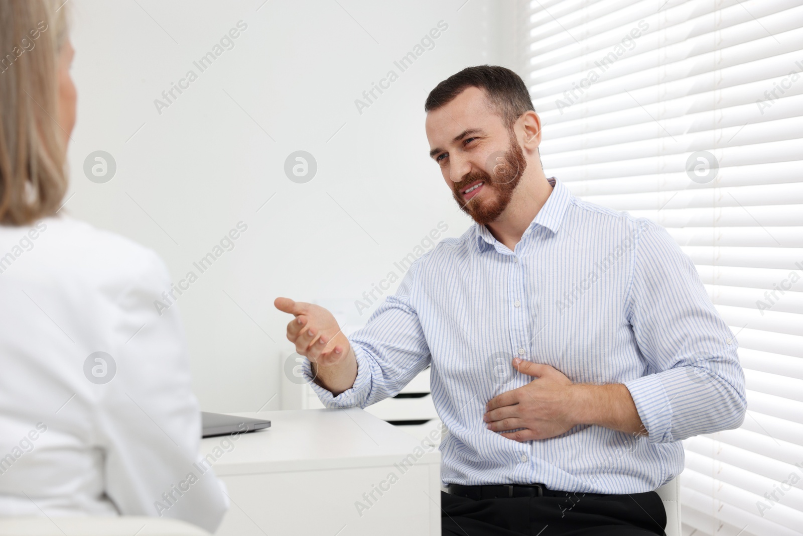 Photo of Doctor consulting patient with stomach pain at table in clinic, closeup