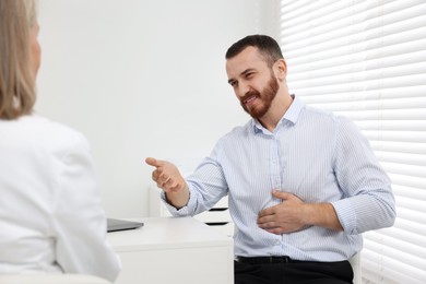 Doctor consulting patient with stomach pain at table in clinic, closeup