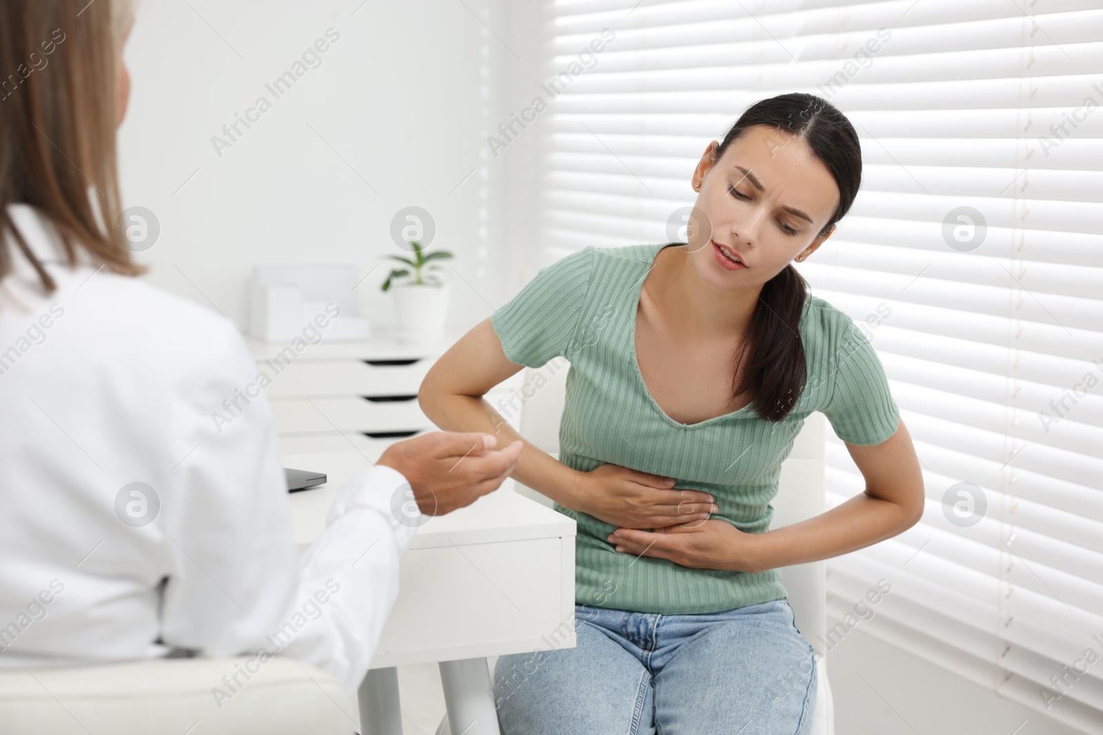 Photo of Doctor consulting patient with stomach pain at table in clinic, closeup