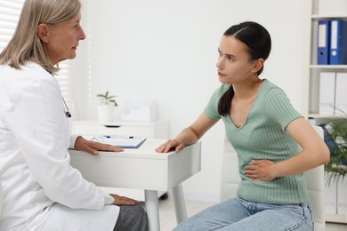 Photo of Doctor consulting patient with stomach pain at table in hospital