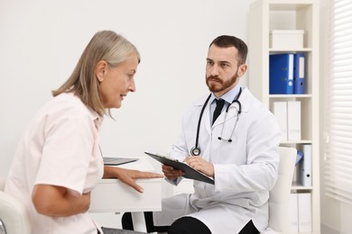 Photo of Doctor consulting senior patient with stomach pain at table in hospital