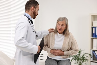 Doctor consulting senior patient with stomach pain in clinic