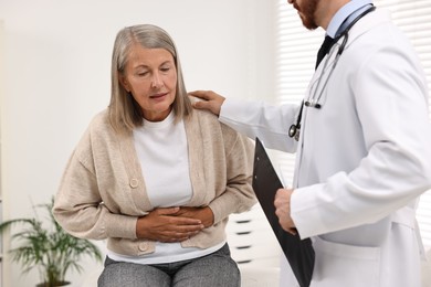 Doctor consulting senior patient with stomach pain in clinic, closeup