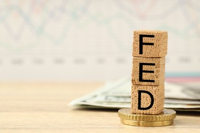 Photo of Stack of cubes with letters Fed (Federal Reserve System), dollar banknotes and coins on wooden table, closeup. Space for text