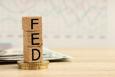 Photo of Stack of cubes with letters Fed (Federal Reserve System), dollar banknotes and coins on wooden table, closeup. Space for text