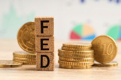 Photo of Stack of cubes with letters Fed (Federal Reserve System) and coins on wooden table, closeup