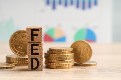 Photo of Stack of cubes with letters Fed (Federal Reserve System) and coins on wooden table, closeup