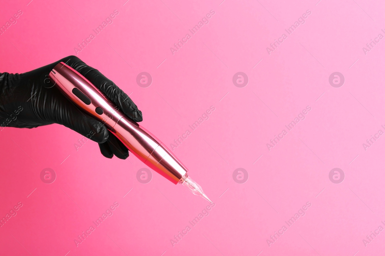 Photo of Professional cosmetologist holding permanent makeup machine on pink background, closeup. Space for text