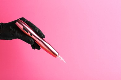 Professional cosmetologist holding permanent makeup machine on pink background, closeup. Space for text