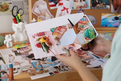 Photo of Creating vision board. Woman cutting out picture at wooden table indoors, closeup