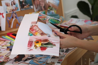 Creating vision board. Woman cutting out picture at wooden table indoors, closeup