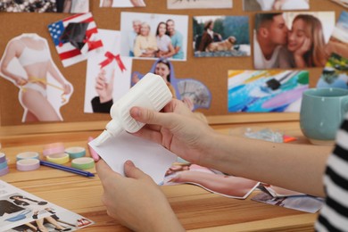 Creating vision board. Woman applying glue onto picture at wooden table indoors, closeup