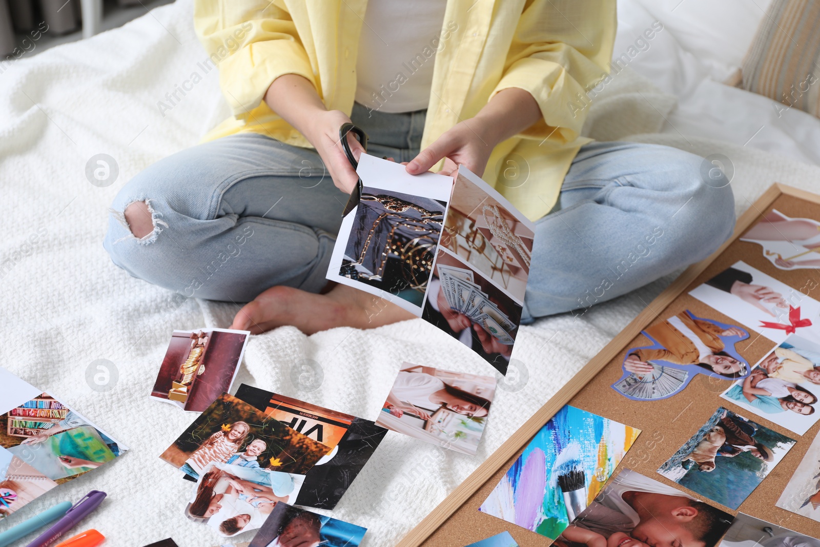 Photo of Creating vision board. Woman cutting out picture on bed indoors, closeup