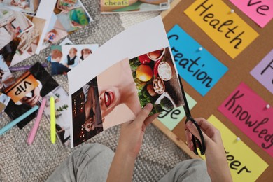 Creating vision board. Woman cutting out picture on floor indoors, top view