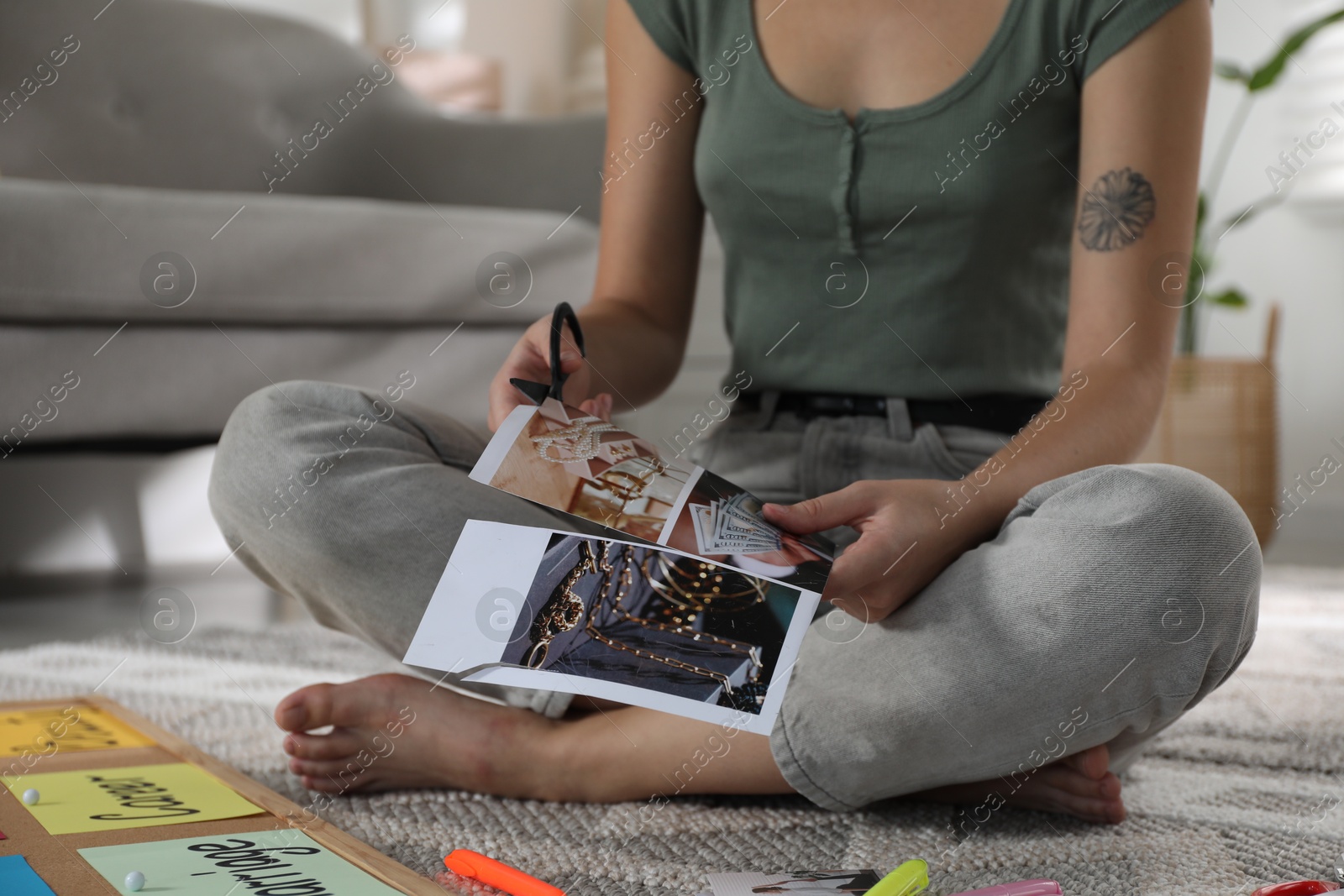 Photo of Creating vision board. Woman cutting out picture on floor indoors, closeup