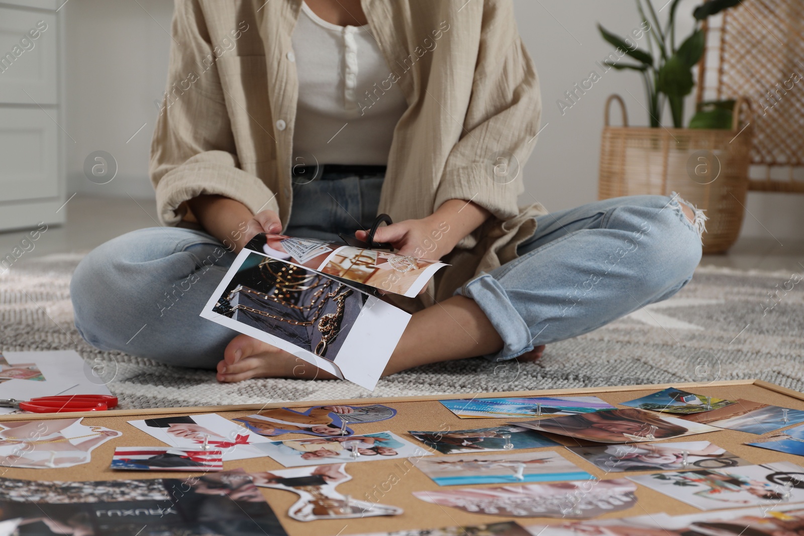 Photo of Creating vision board. Woman cutting out picture on floor indoors, closeup