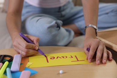 Creating vision board. Woman writing word Travel on card table indoors, closeup