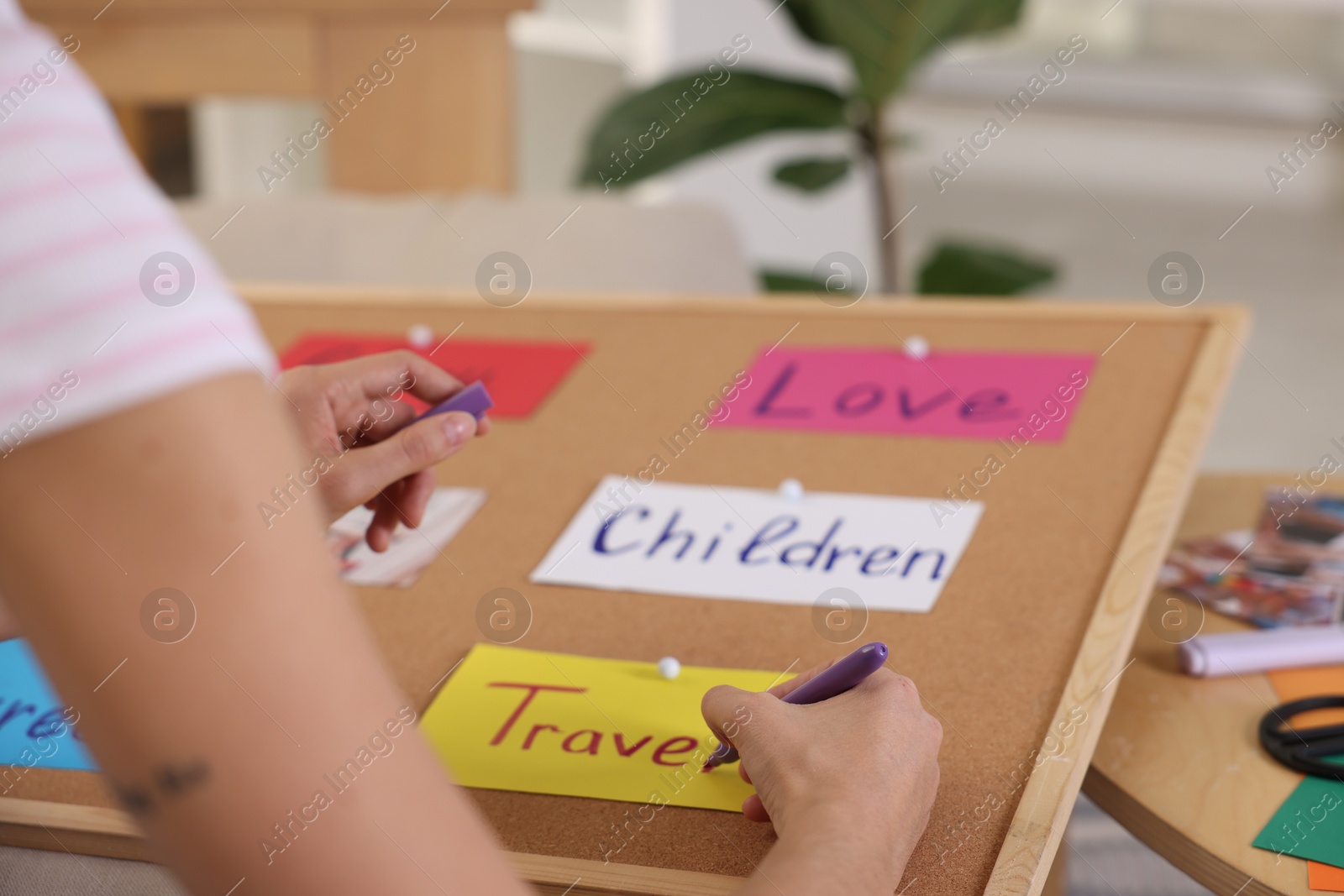 Photo of Creating vision board. Woman writing word Travel on card indoors, closeup