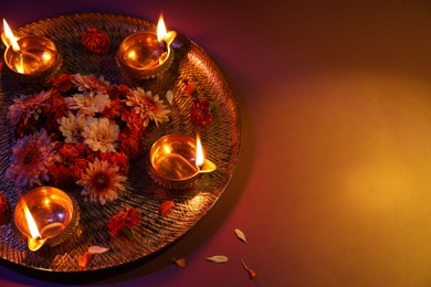 Photo of Diwali celebration. Diya lamps and beautiful flowers on color background, space for text