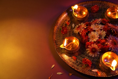 Diwali celebration. Diya lamps and beautiful flowers on color background, space for text