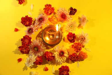 Photo of Diwali celebration. Diya lamp and beautiful flowers on yellow background, flat lay