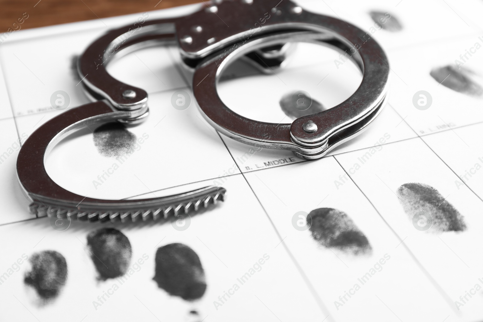 Photo of Human fingerprints and handcuffs on paper, closeup. Criminal conviction