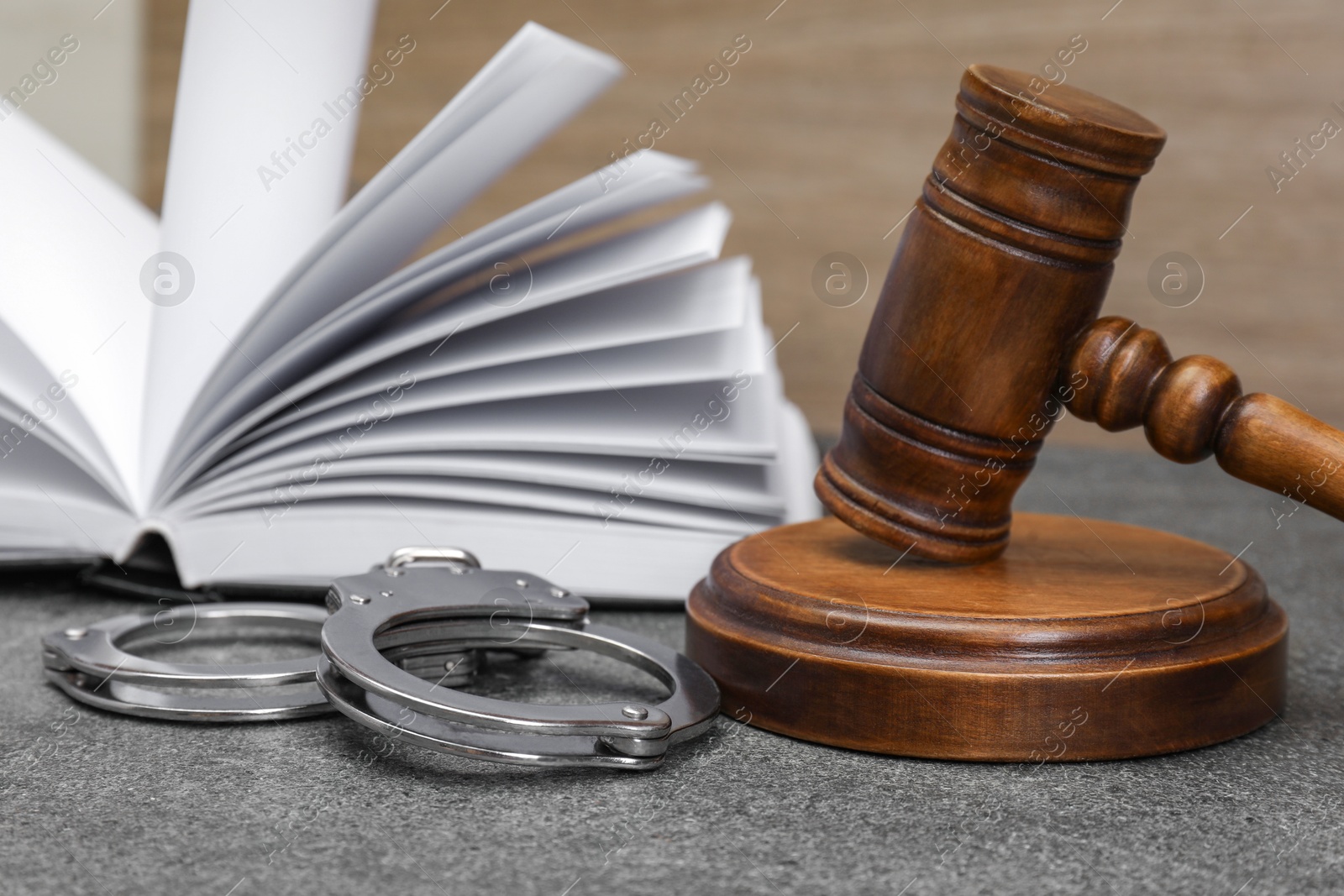 Photo of Book, judge's gavel and handcuffs on gray textured table, closeup