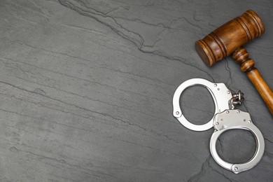 Photo of Judge's gavel and handcuffs on gray textured table, flat lay. Space for text