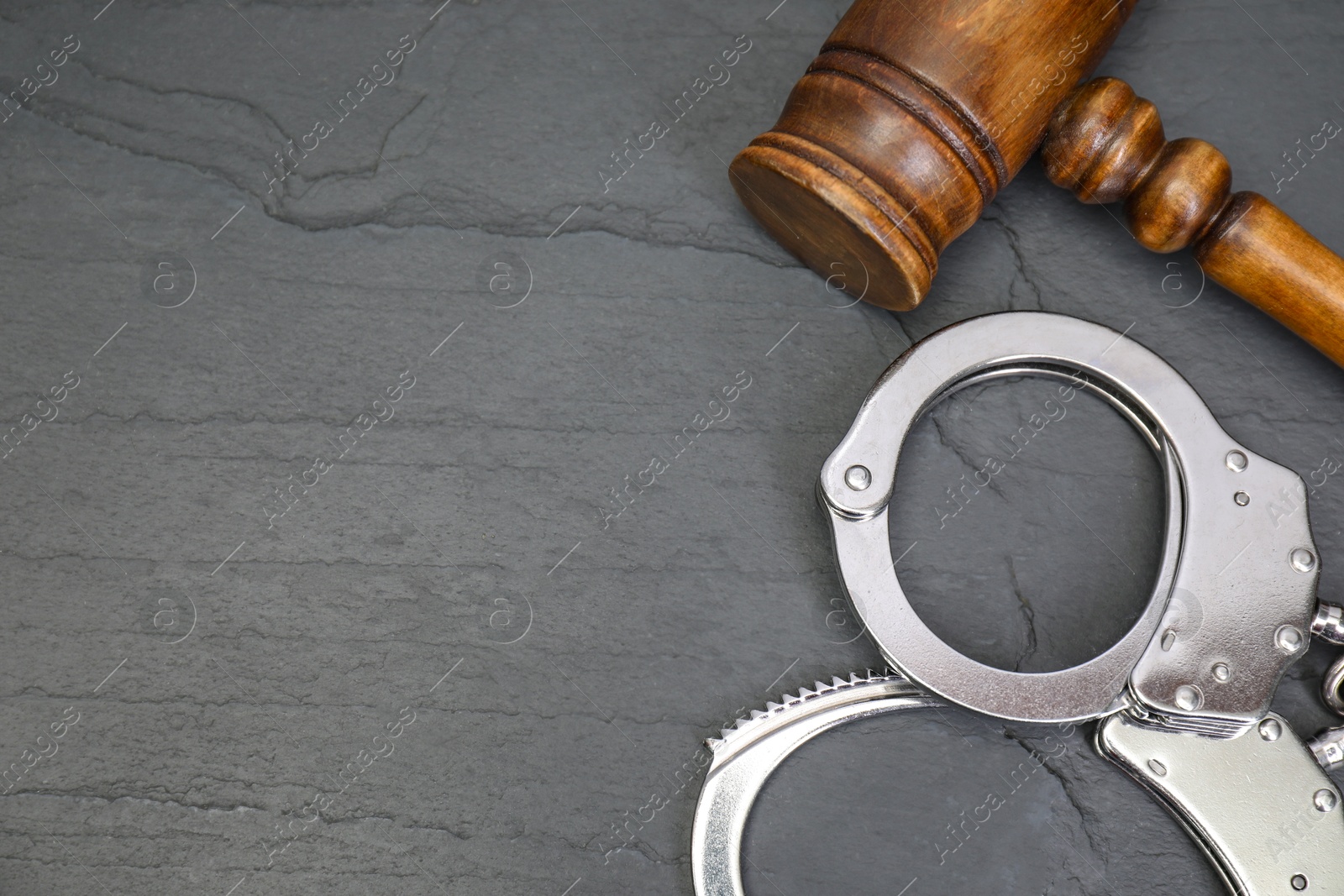 Photo of Judge's gavel and handcuffs on gray textured table, flat lay. Space for text