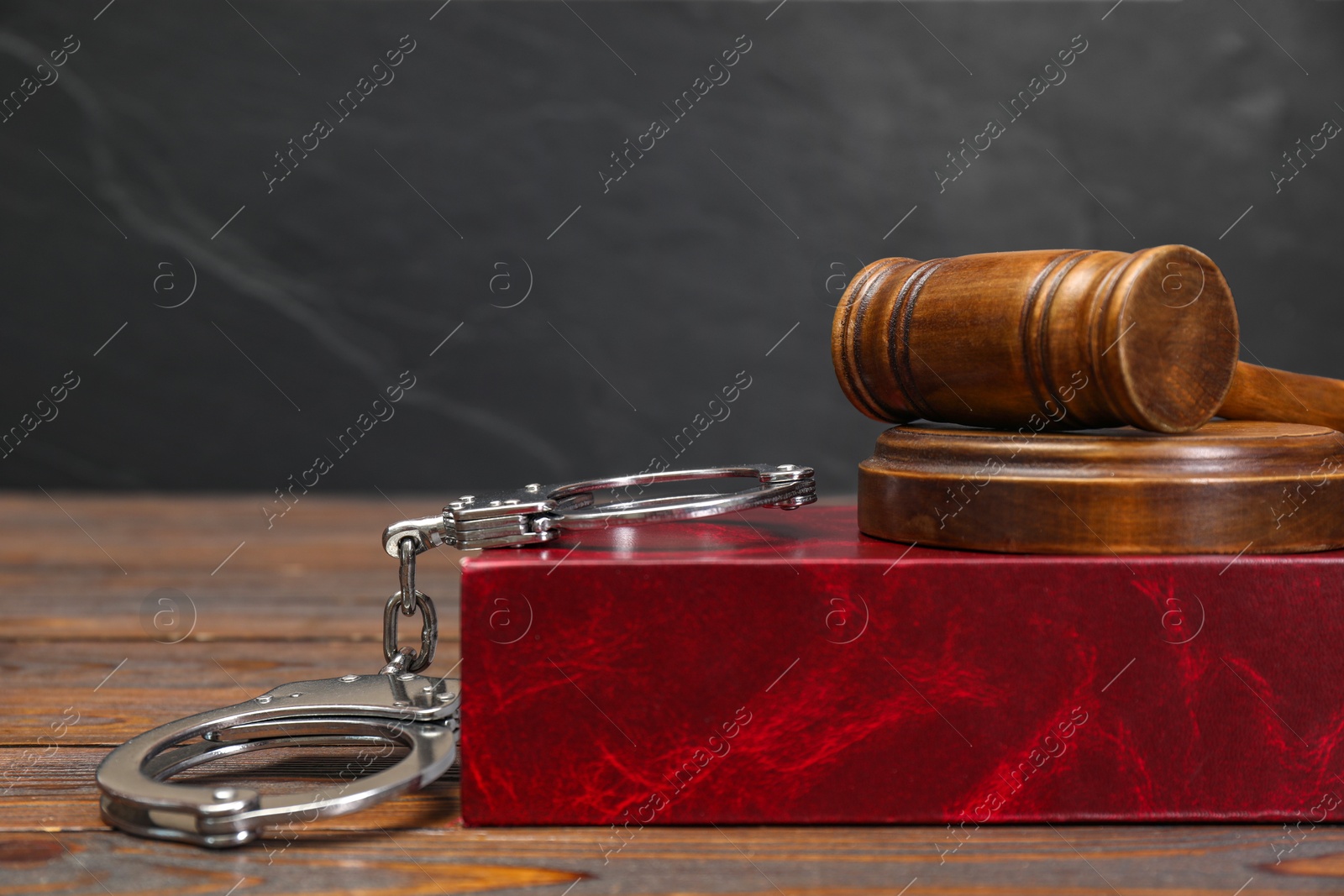 Photo of Book, judge's gavel and handcuffs on wooden table against gray background, space for text