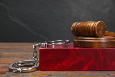 Book, judge's gavel and handcuffs on wooden table against gray background, space for text