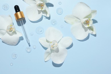 Photo of Beautiful orchid flowers and dropper with cosmetic product in water on light blue background, flat lay