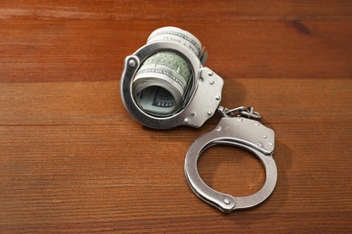 Handcuffs with dollar banknotes on wooden table